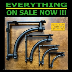 May include: Set of five black metal corner brackets with a curved design. The brackets are arranged in descending size order. The largest bracket is 12 inches wide and the smallest is 6 inches wide.  The brackets are made by Tuscan Iron.
