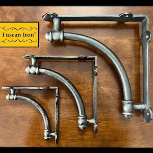 May include: Set of three metal shelf brackets with a curved design. The brackets are made of iron and have a silver finish. The brackets are in different sizes and are arranged from largest to smallest.
