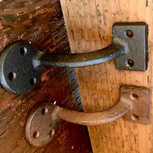 Puede incluir: Dos soportes de estante de hierro fundido, uno negro y otro marr&oacute;n, montados en una superficie de madera.
