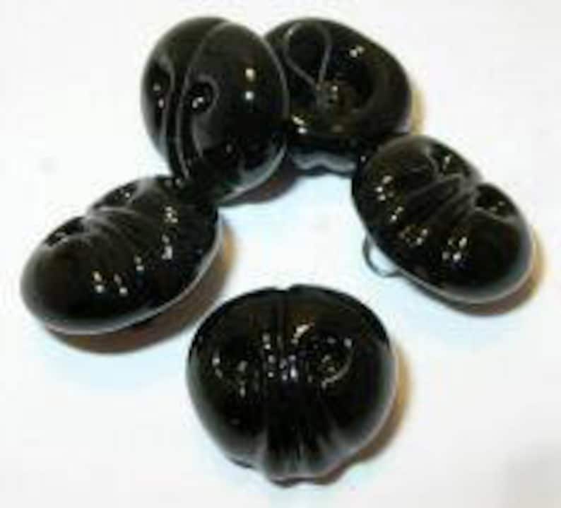 May include: Four black plastic buttons with a raised design. The buttons are round and have a shiny finish.