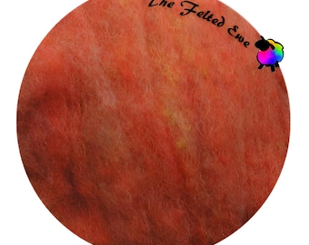 May include: A round, orange-red felted wool roving with subtle yellow and brown highlights. The roving is labeled "The Felted Ewe" with a small cartoon sheep logo.