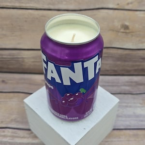 May include: Purple grape-flavored soda can candle with a white wax top and a lit wick. The can has the word "FANTA" printed on it in blue and white letters.