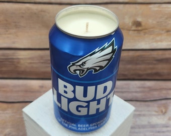 May include: A blue and white Bud Light can candle with a Philadelphia Eagles logo. The candle is on a white wooden block.