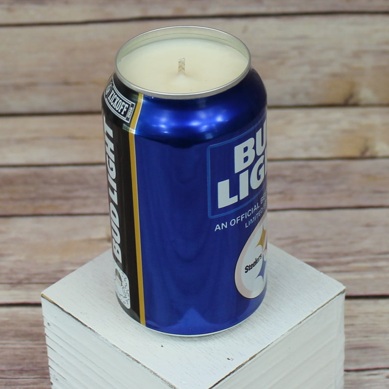 May include: A blue and white can shaped candle with the text "Bud Light" and "An Official Licensed Product" on the side. The candle is lit and has a white wax top.
