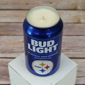 May include: A blue and silver can candle with a white wax top. The can has the text "Bud Light" and "An Official Beer Sponsor Limited Edition". The can also has a Pittsburgh Steelers logo.