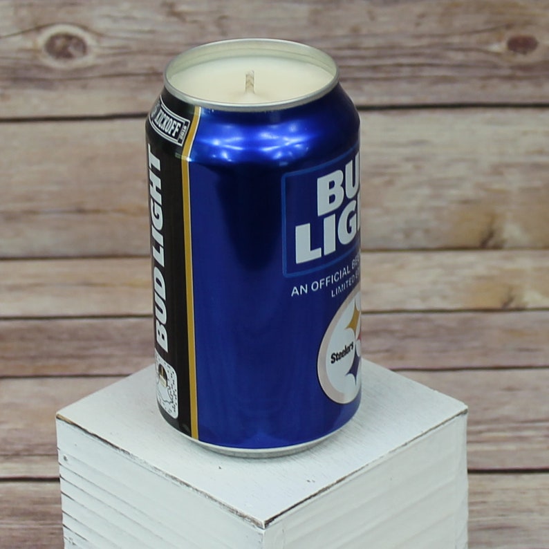 May include: A blue and white Bud Light can candle with a Steelers logo. The candle is on a white wooden stand.