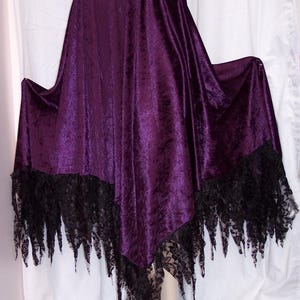 May include: A dark purple velvet skirt with a black lace trim. The skirt features a wide black lace waistband and a handkerchief hemline with jagged black lace edging. The fabric has a soft, textured appearance.