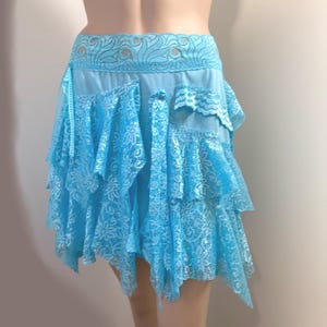 Può includere: Gonna in pizzo azzurro con design a strati. La gonna presenta un motivo floreale dettagliato in pizzo e un bordo smerlato in pizzo in vita. L'orlo asimmetrico è creato da più strati di pizzo.