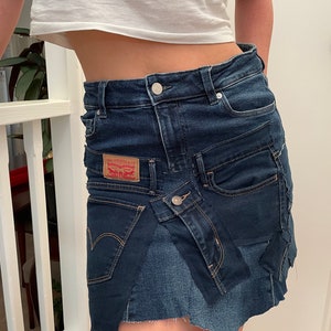 May include: A dark blue denim skirt with a patchwork design. The skirt features a Levi Strauss & Co. label and a raw hemline. The skirt has a button closure and pockets.
