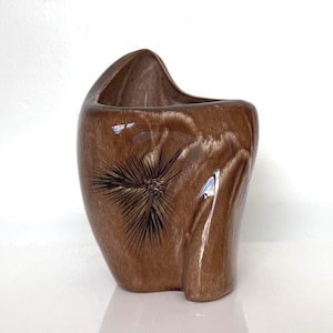 May include: A brown ceramic vase with a unique, organic shape. The vase features a textured surface and a stylized floral design. The interior is smooth and dark, contrasting with the exterior's rough texture. A decorative piece for the home.