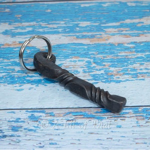 May include: A black metal bottle opener keychain with a twisted design. The keychain is on a blue wooden surface. The number "1" is visible in the upper right corner of the image.