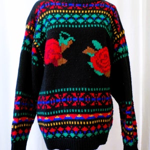 Puede incluir: Suéter de punto negro con un patrón geométrico colorido y dos rosas rojas en la parte delantera.