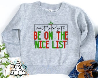 May include: A light gray sweatshirt with the text "most likely to BE ON THE NICE LIST" in red and green. The sweatshirt is paired with blue jeans and brown shoes.