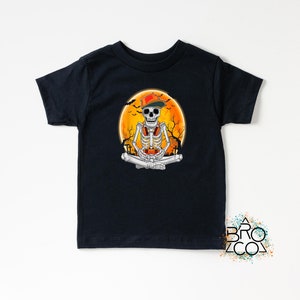 May include: Black t-shirt featuring a skeleton wearing a red and green cap and headphones, sitting in a meditative pose. The skeleton is in front of an orange moon with trees and bats. The shirt has the text "ABROZCO" in the bottom right corner.