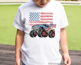 Könnte beinhalten: Ein weißes T-Shirt mit kurzen Ärmeln und einem Grafikdruck eines blauen Monstertrucks mit roten und weißen Streifen, großen schwarzen Reifen und einer kleinen amerikanischen Flagge. Dahinter ist eine verwaschene US-Flagge in Rot, Weiß und Blau.
