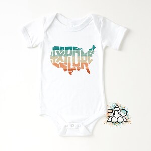 May include: A white short-sleeve baby bodysuit featuring a graphic of the United States map filled with the word EXPLORE in a distressed, horizontal striped pattern of teal, beige, and orange. A small logo with the text BRO CO is visible.