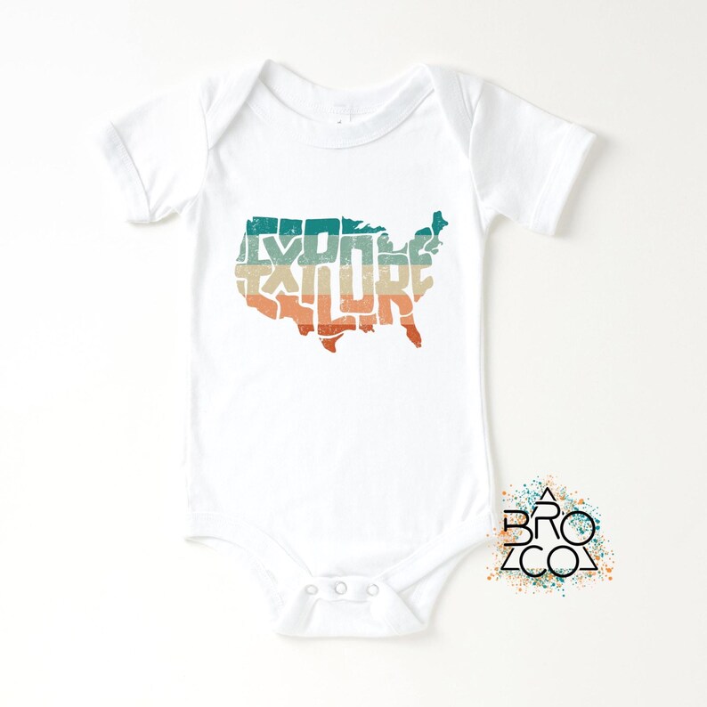 May include: A white short-sleeve baby bodysuit featuring a graphic of the United States map filled with the word EXPLORE in a distressed, horizontal striped pattern of teal, beige, and orange. A small logo with the text BRO CO is visible.