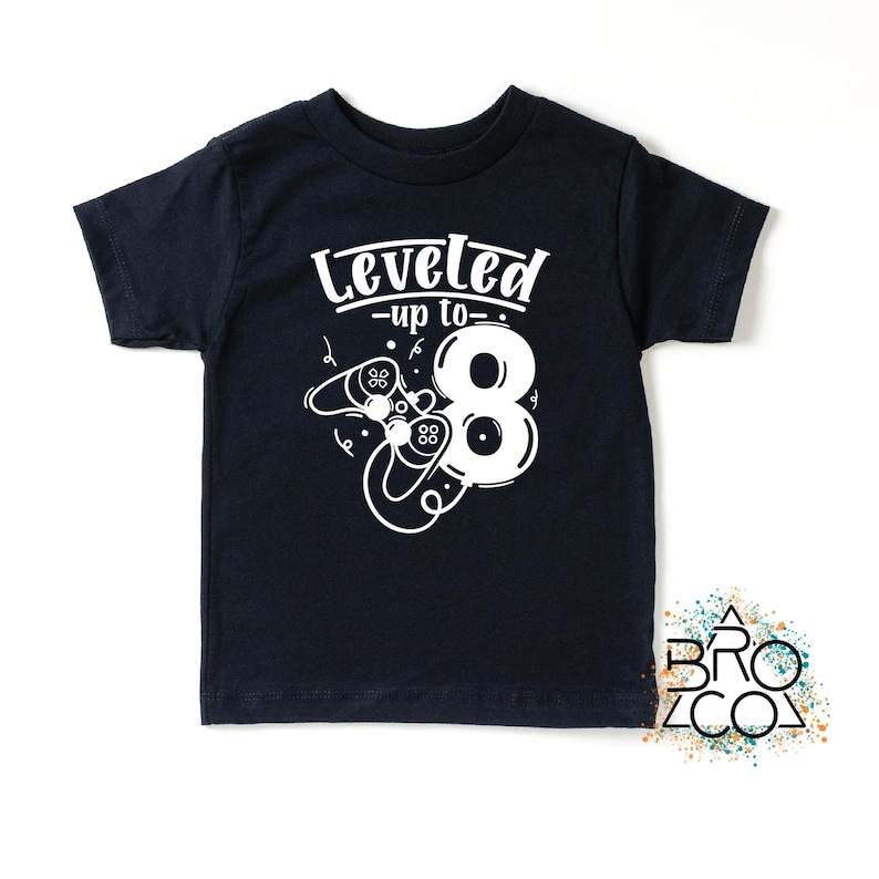 May include: A navy blue t-shirt featuring the text "Leveled up to 8" in white, along with a number 8 and game controller graphics. This t-shirt is designed for children.
