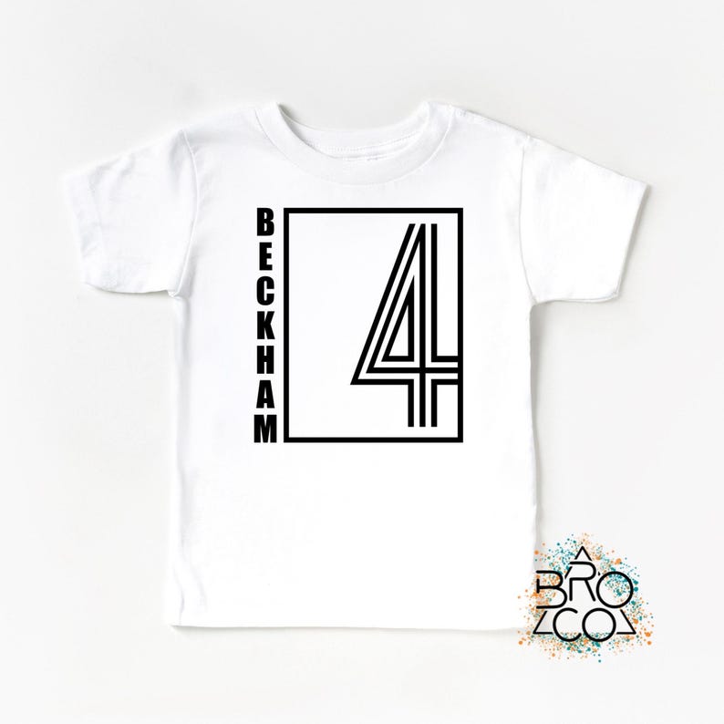 May include: A white short-sleeved t-shirt featuring a black graphic design on the chest. The design consists of the word BECKHAM written vertically in a sans-serif font next to a large number 4 enclosed within a black rectangular frame.