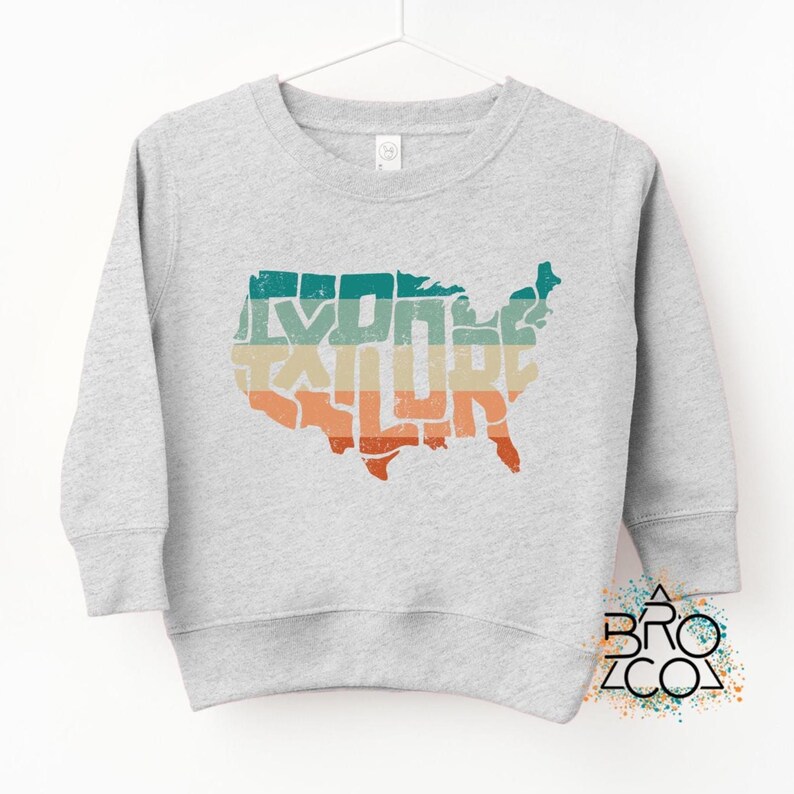 May include: A light gray long-sleeve sweatshirt featuring a distressed graphic of the United States map filled with horizontal stripes in teal, beige, and orange. The word EXPLORE is integrated into the map design in a bold, blocky font.