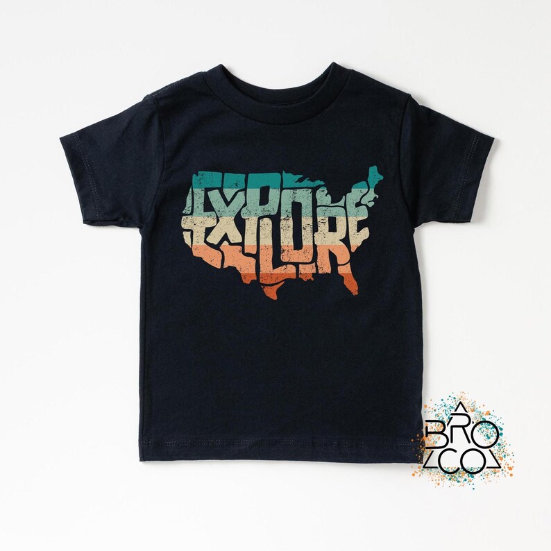 May include: A black short-sleeve t-shirt featuring a graphic of the United States map filled with the word EXPLORE in a distressed, multi-colored horizontal striped pattern of teal, beige, and orange. The design has a weathered texture.