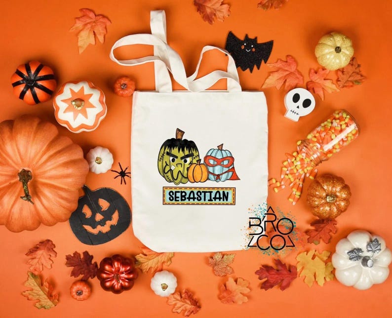 Puede incluir: Un bolso tote color crema con un dise&ntilde;o de Halloween con dos calabazas de dibujos animados y el nombre "Sebastian". La bolsa est&aacute; rodeada de calabazas, hojas y decoraciones de Halloween sobre un fondo naranja.