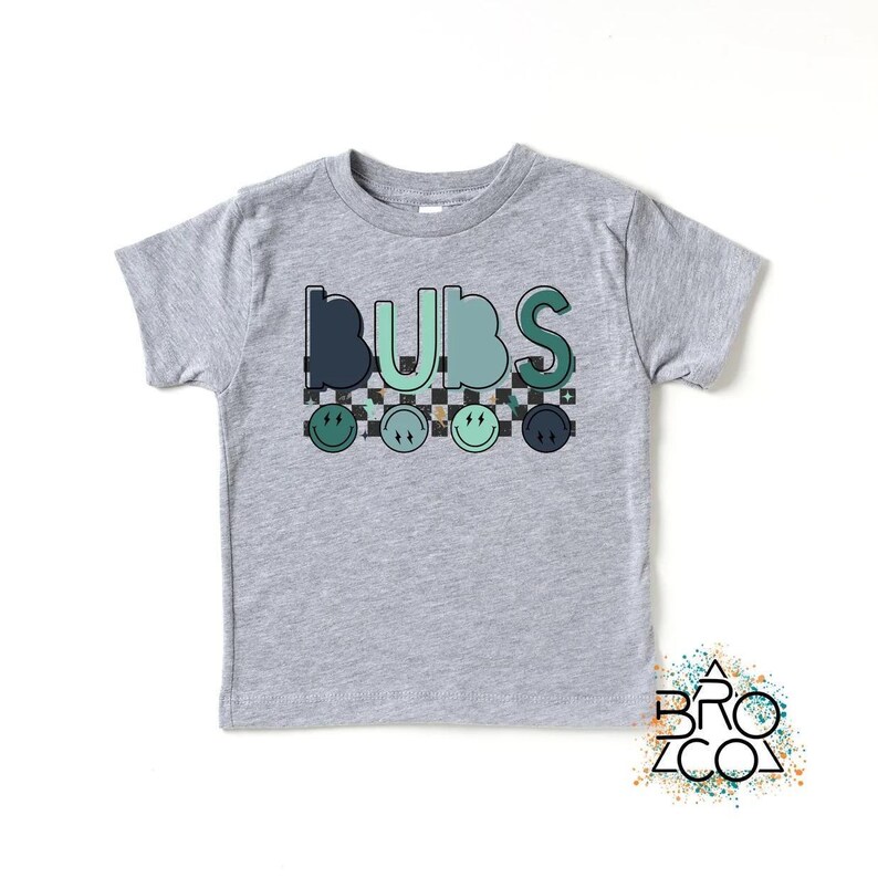 May include: A grey short-sleeved t-shirt with the word "BUBS" printed in green, blue, and black letters. The letters are outlined in black and have a checkered pattern behind them. There are five green, blue, and black smiley faces below the word.