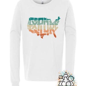 May include: A white long-sleeve shirt featuring a graphic of the United States map filled with the word EXPLORE in a distressed, horizontal striped pattern of teal, beige, and orange. A logo with the text BRO CO is in the bottom corner.