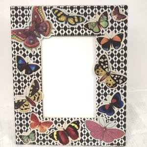 May include: A rectangular picture frame with a black and white diamond pattern. Colorful butterfly stickers are arranged around the frame. The butterflies have various colors, including red, blue, yellow, and green.