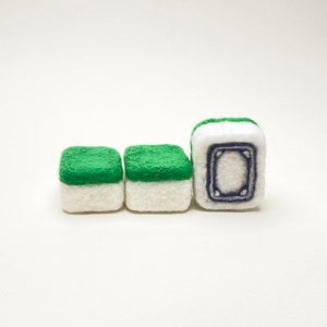 May include: Three felt dice with green tops and white bottoms. The die on the right has a black and blue design on the side.