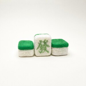 May include: Three white and green felt mahjong tiles. The centre tile has the Chinese character "發" in green.