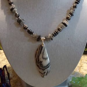 May include: A black and white striped stone pendant necklace with a silver chain and black and white beads. The necklace is displayed on a white mannequin bust.