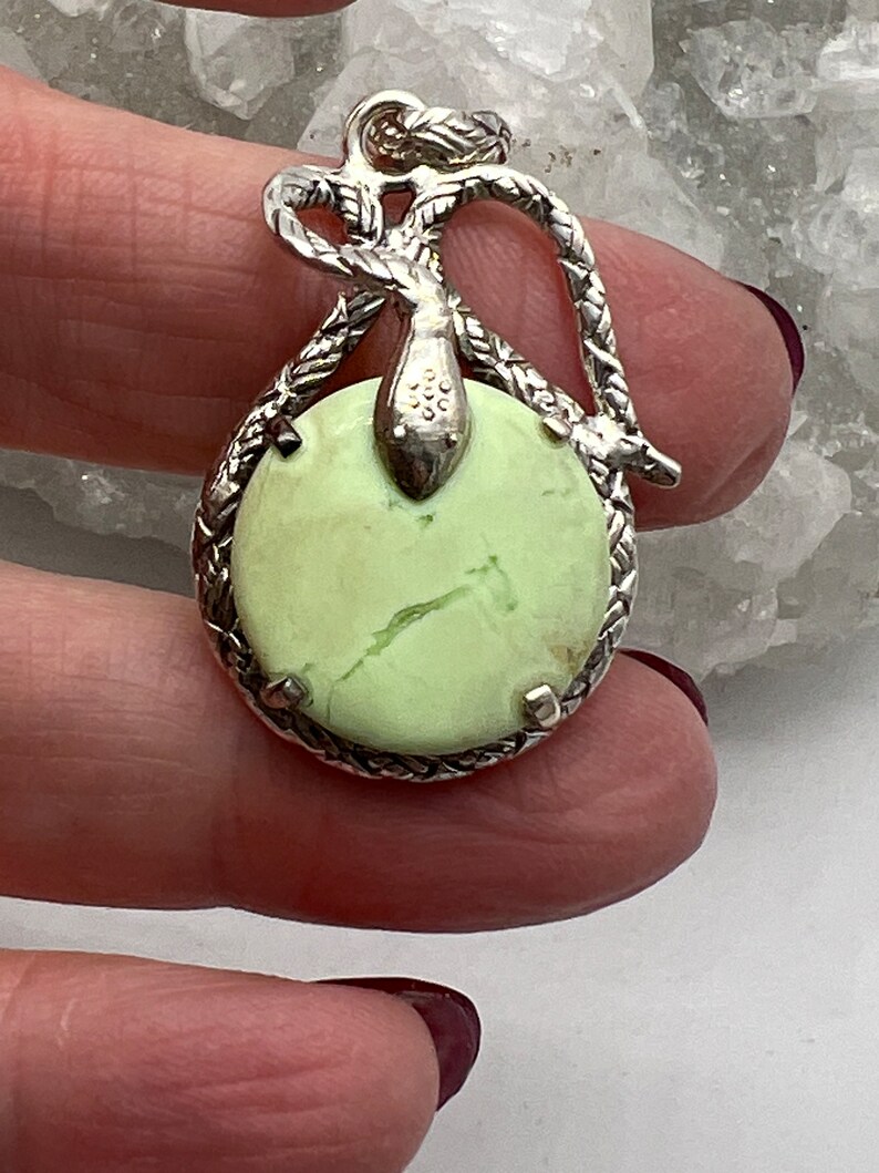May include: A silver pendant with a green serpentine stone set in a rope-like design. The pendant features a snake design with a knotted tail.