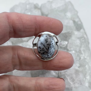May include: A silver ring with a white and black dendritic agate stone. The stone is oval shaped and set in a silver band.
