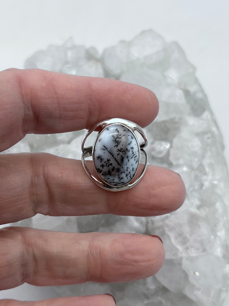 May include: A silver ring with a white and black dendritic agate stone. The stone is oval shaped and set in a silver band.