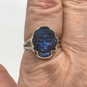 May include: A silver ring with a blue stone carved into the shape of a Buddha's face.