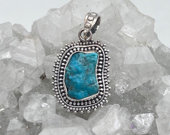 May include: A turquoise stone pendant with a silver setting. The pendant is surrounded by a decorative border of small silver beads.