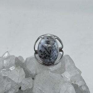 May include: A silver ring with a dendritic agate stone set in a bezel setting. The stone is a light gray with black dendritic patterns.