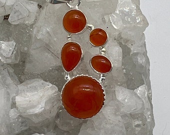 May include: A silver pendant with five orange carnelian stones. The stones are set in a cluster and are surrounded by a silver frame. The pendant is on a white background.