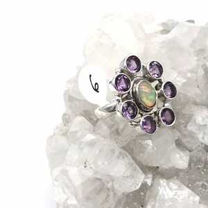 May include: A silver ring with a large opal gemstone surrounded by smaller amethyst gemstones.