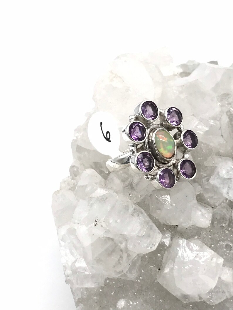 May include: A silver ring with a large opal gemstone surrounded by smaller amethyst gemstones.