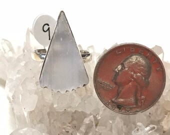 May include: A silver ring with a triangular selenite stone. The ring is shown on a bed of clear quartz crystals. A US quarter is shown for size comparison.