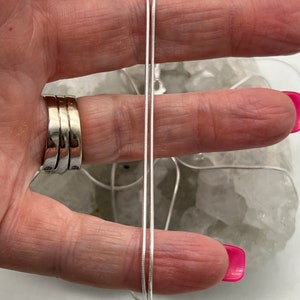 May include: A delicate silver necklace with a thin, snake chain design. The necklace is displayed against a neutral background, highlighting its simple elegance. The chain is approximately 20 inches long.