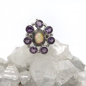 May include: A silver ring with a white opal gemstone surrounded by eight purple amethyst gemstones.