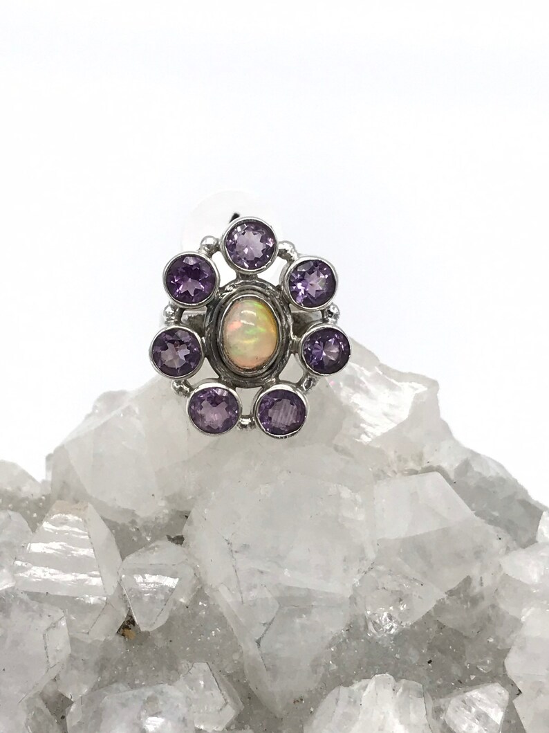 May include: A silver ring with a white opal gemstone surrounded by eight purple amethyst gemstones.