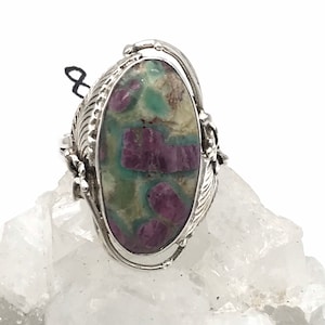 Op de afbeelding: Een zilveren ring met een ovale groene en roze edelsteen, gezet in een gedetailleerde zilveren setting.