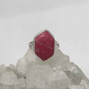 Peut inclure: Une bague en argent avec une pierre précieuse en rhodochrosite rose. La pierre précieuse est de forme hexagonale avec une taille facetée.