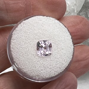 May include: A pale pink cushion-cut gemstone in a small white foam container.