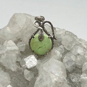 May include: A silver pendant featuring a green gemstone set in a snake design.