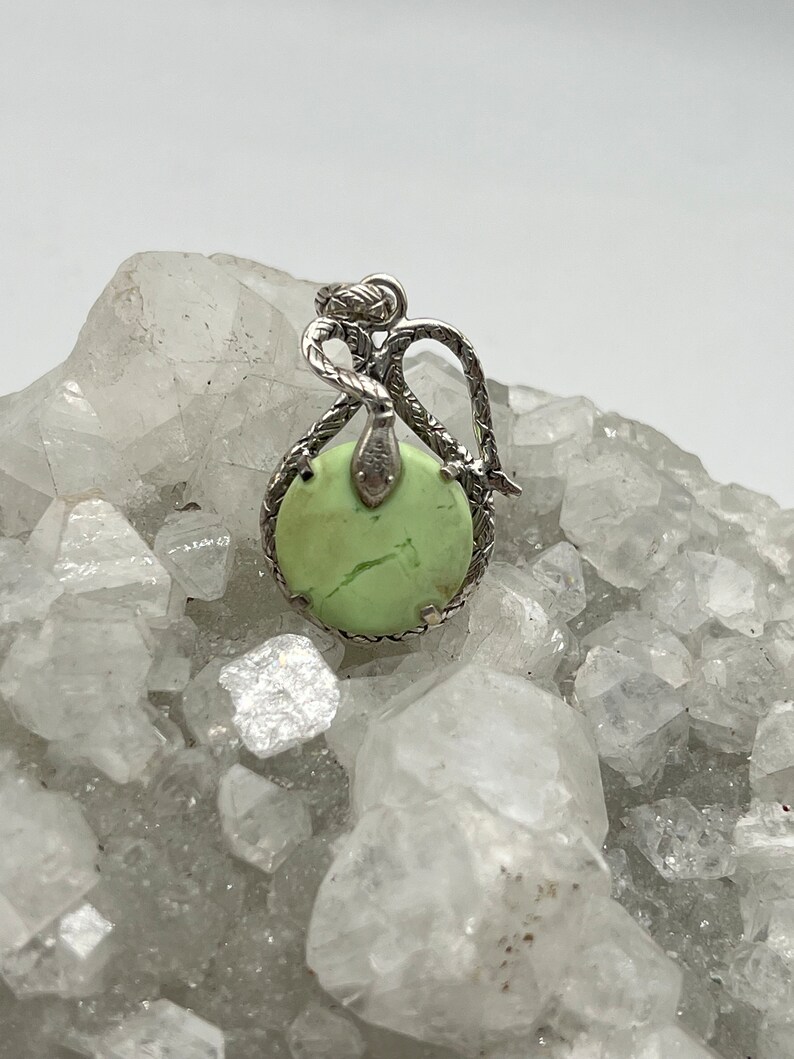 May include: A silver pendant featuring a green gemstone set in a snake design.
